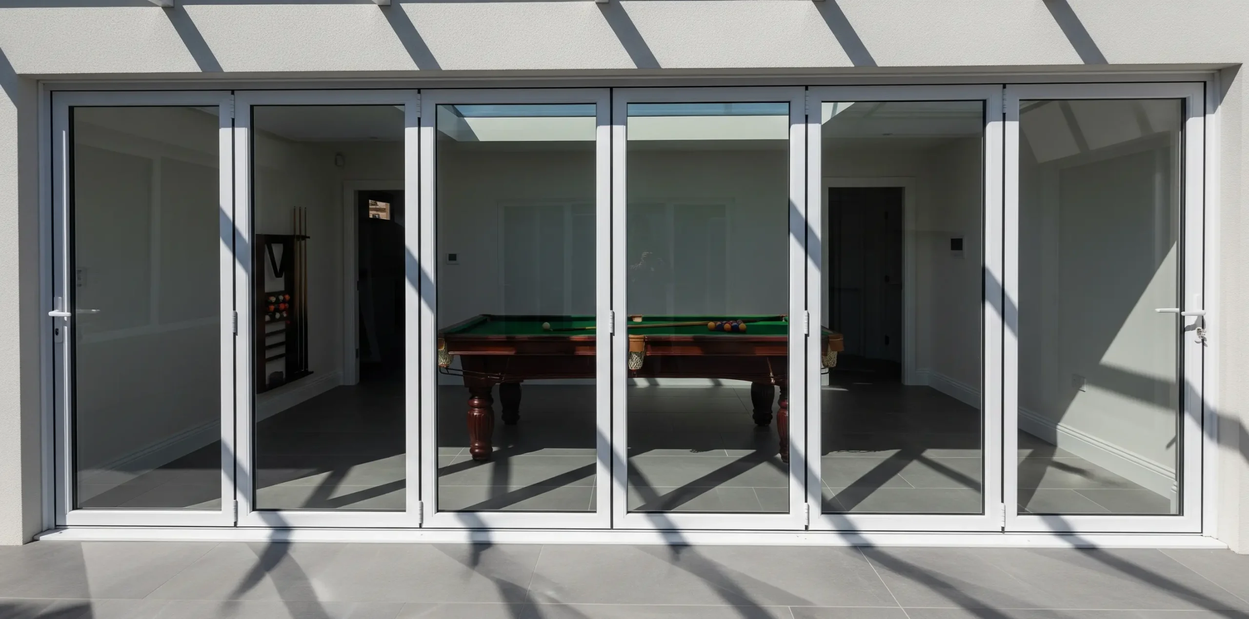 White-framed bi-fold doors enclosing a room containing a pool table, with the exterior patio structure visible above.