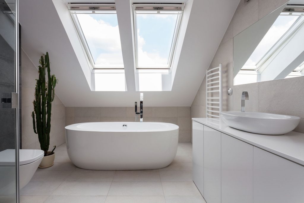 Modern attic bathroom with freestanding tub and two skylight windows.