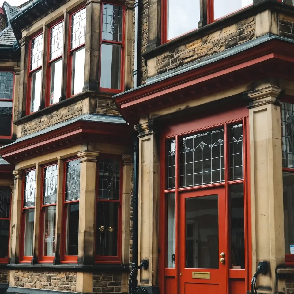 Victorian brownstone building facade with striking red window frames and door.